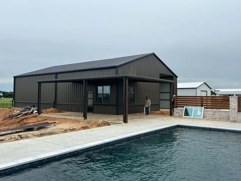 Dark brown metal barndominium with a covered patio behind a newly filled swimming pool