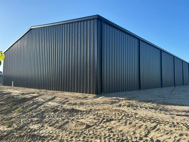 Gable end of a large dark brown metal shop on a fresh concrete slab