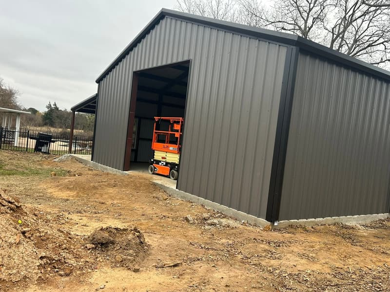 Dark brown metal workshop with a scissor lift parked inside the open roll-up door