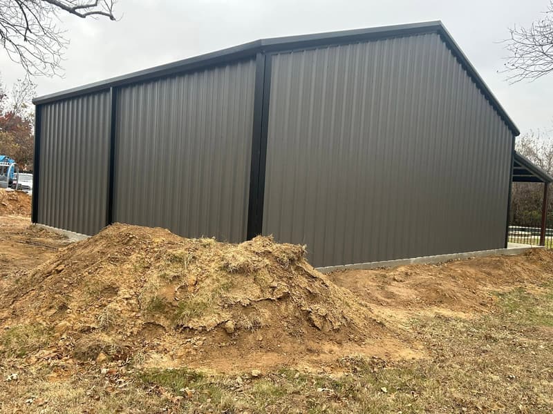 Long side wall of a dark brown metal workshop with fresh dirt work in front