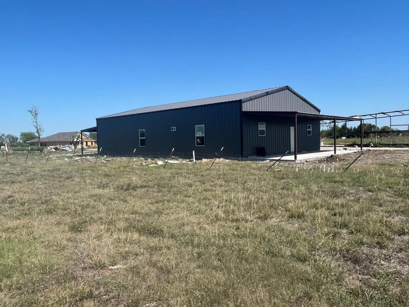 Charcoal metal barndominium with a covered porch on open pasture, seen from the field
