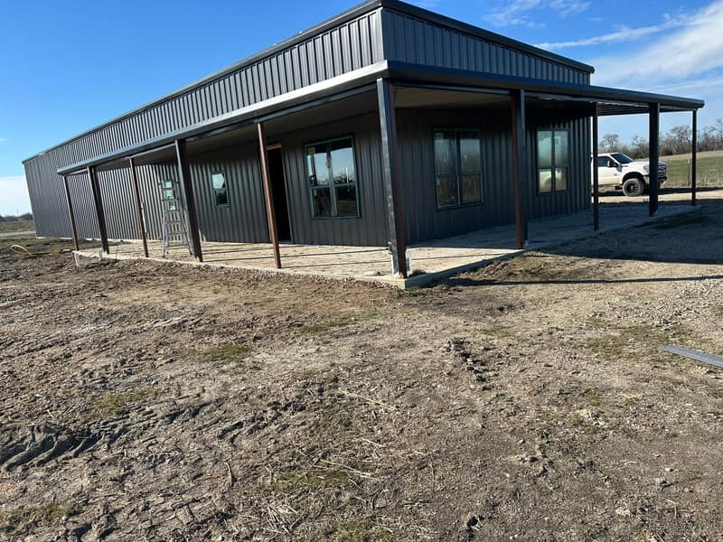 Charcoal metal barndominium with a wraparound covered porch on red steel posts