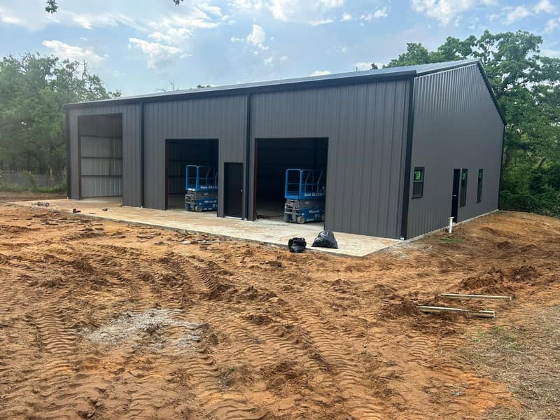 Charcoal metal shop with two tall bay openings and lifts parked inside, dirt work in front