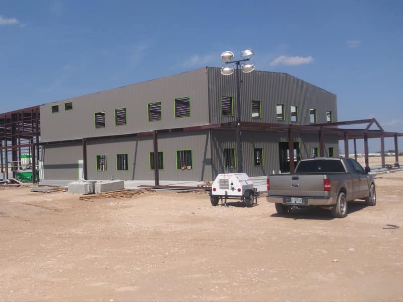 Two-story tan commercial metal building with the steel frame of a covered wing still open