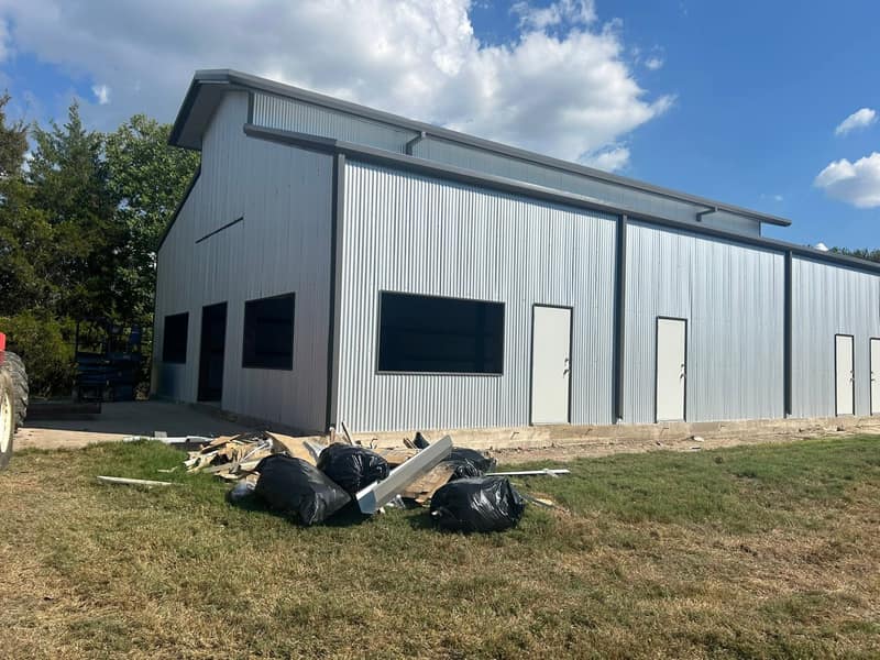 Light gray metal shop with black trim, two bay openings and a walk door, seen from the front