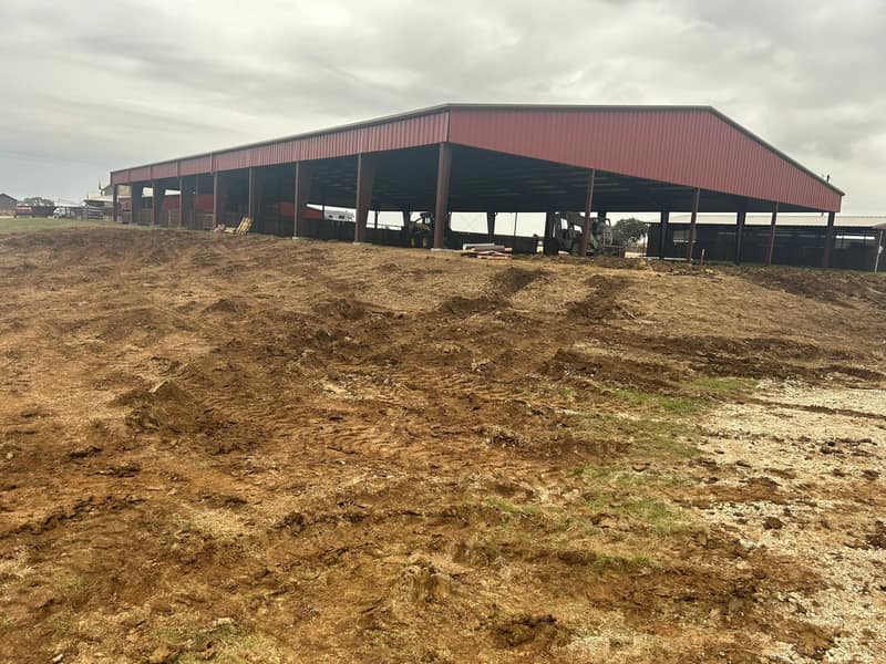 Red open-sided metal arena cover from the corner, graded dirt in the foreground