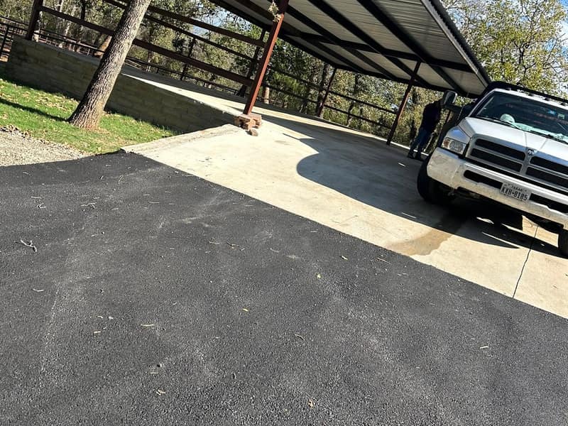 Steel carport canopy on black posts over a fresh asphalt drive, pickup parked underneath