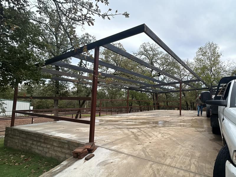 Steel carport frame with purlins set, roof panels still to come, vehicles parked underneath
