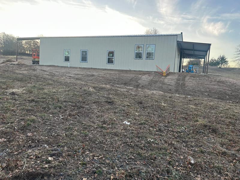 Long tan metal building with blue trim and a covered porch, seen from across the open field
