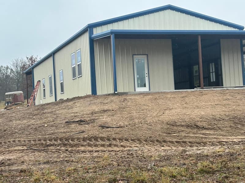 Gable end of a tan metal building with blue trim and a covered lean-to, viewed from the slope