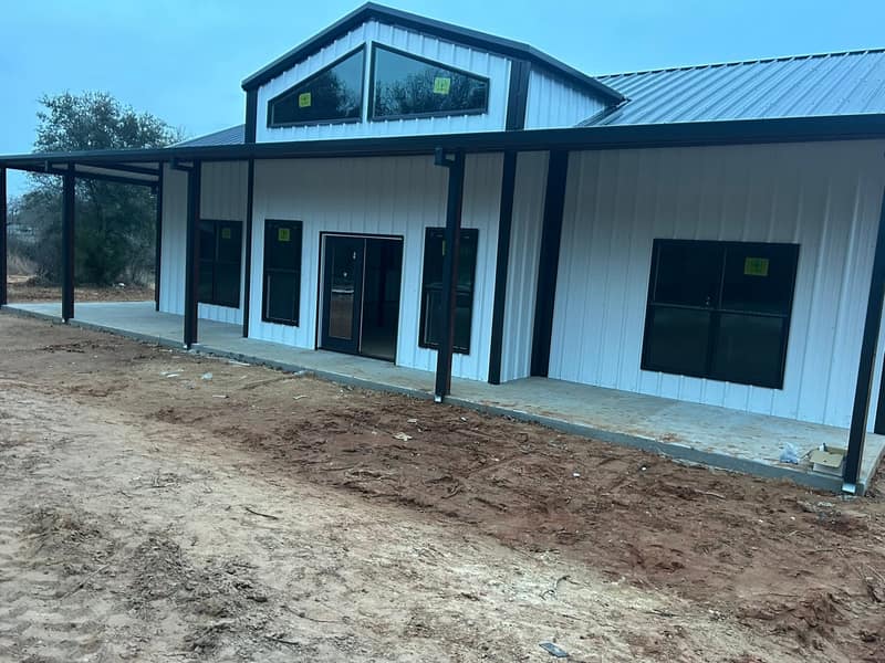 Front of a white metal barndominium with black porch posts, a glass entry door and a gable window