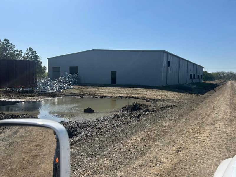 White metal commercial building at the end of a dirt road, water standing in the ruts