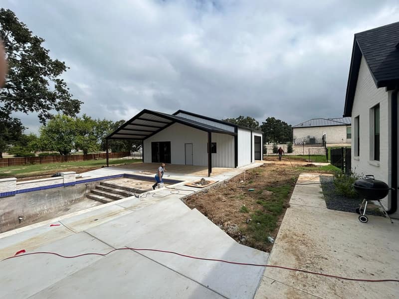 White metal pool house with a dark roof next to a swimming pool under construction