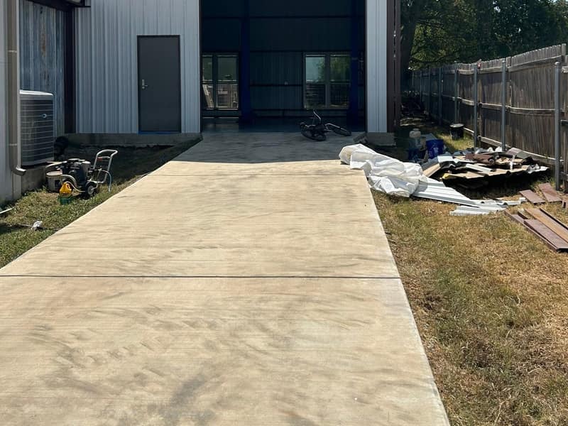 White metal pool house with an open bay and walk door on a new concrete pad, cedar fence alongside