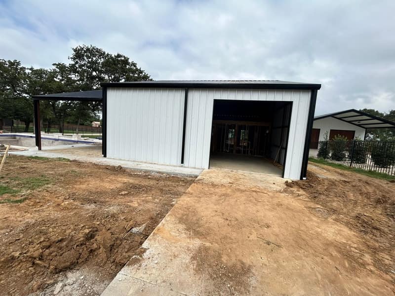 White metal pool house with black trim and an open front bay, dirt graded for the drive