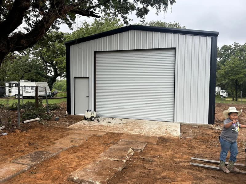 White metal shop with black trim, a white roll-up door and a walk door, Lorenzo standing in front