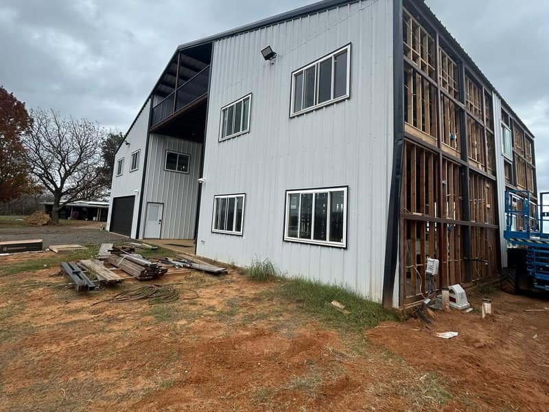Side of a two-story white metal barndominium with the wood framing of the wall still exposed