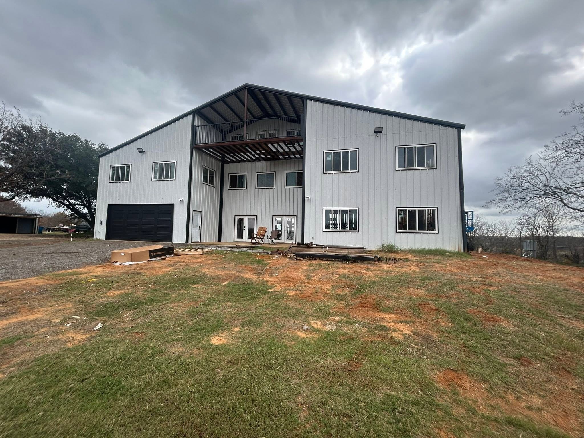 Two-story white barndominium with a covered balcony under a stormy sky