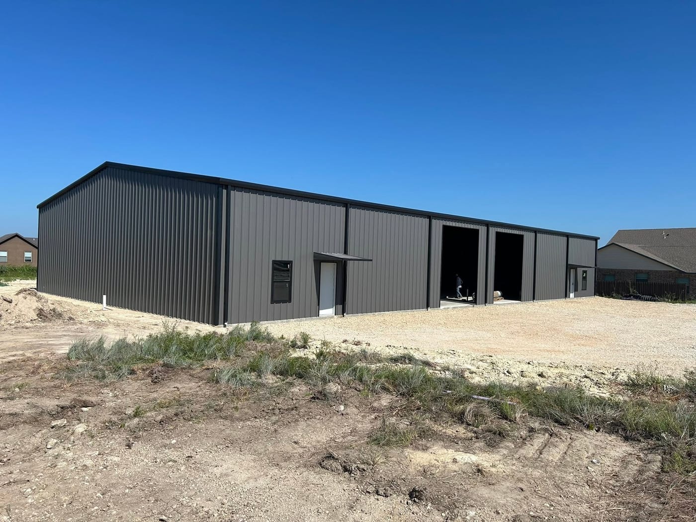 Gray metal warehouse on a cleared lot under a blue sky