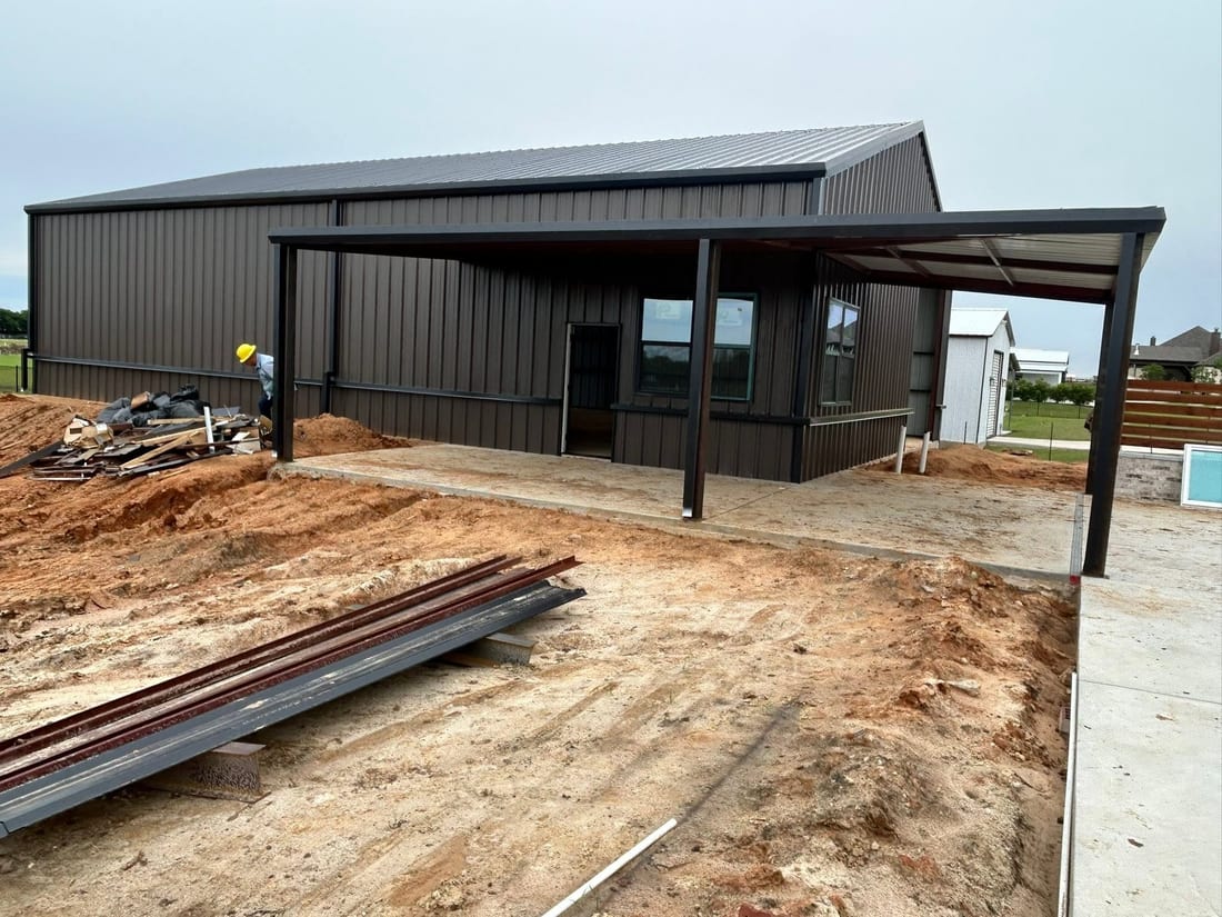 Brown metal storage building with an open lean-to and steel stacked in front