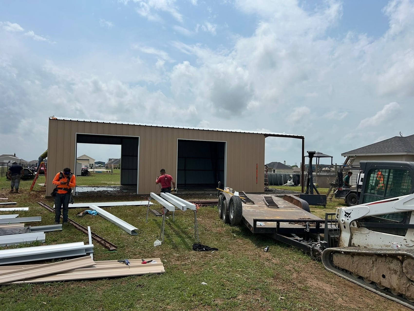 Lorenzo Galvan and his crew erecting a tan metal building beside a skid steer and trailer