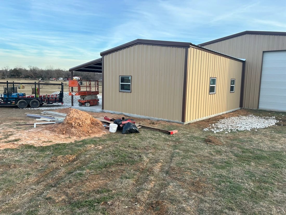 Tan metal storage building with a lean-to and a tractor alongside