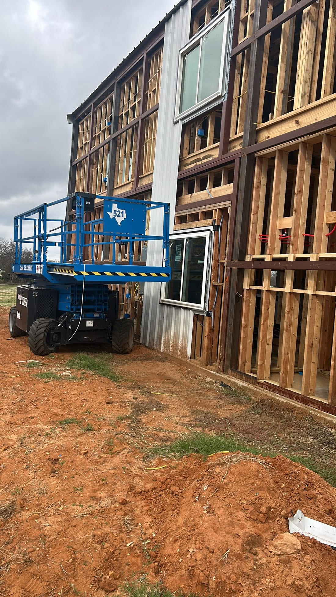 Blue scissor lift beside a metal building being framed out